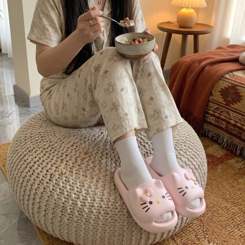 Person sitting on a bean bag chair eating from a bowl, wearing pink slides with cat designs.